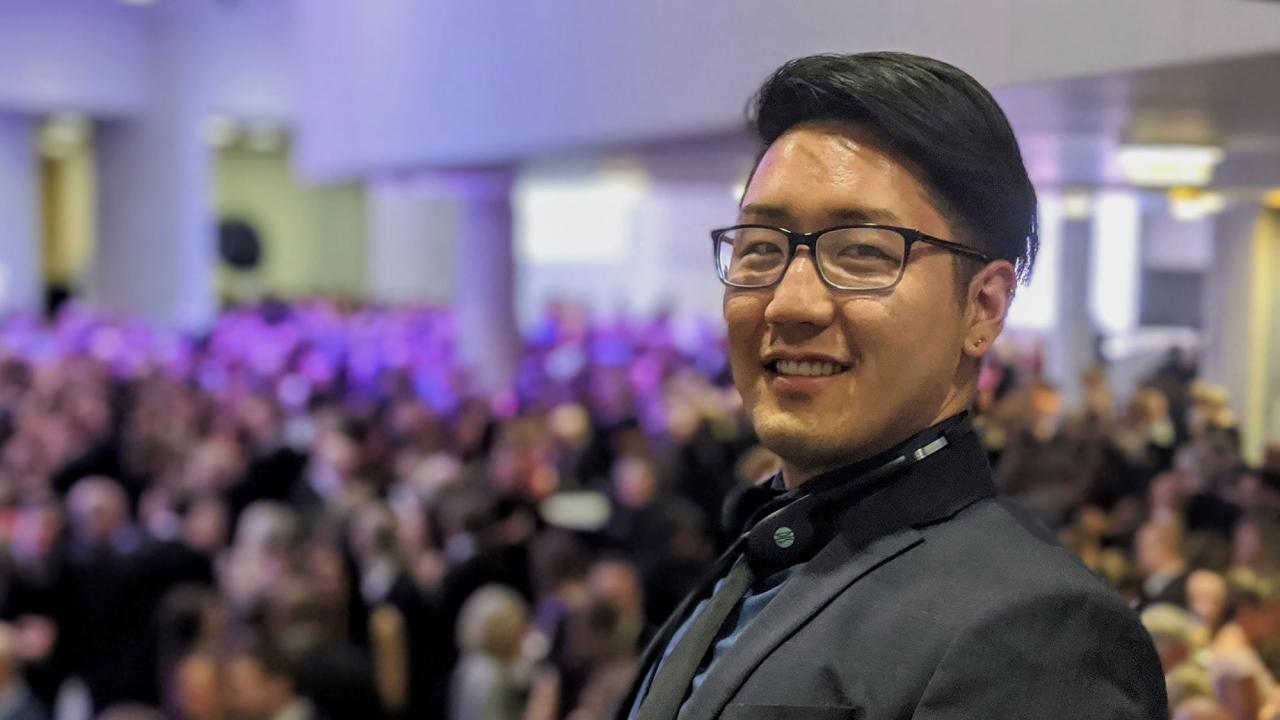 Smiling man with glasses and headphones before a blurred audience