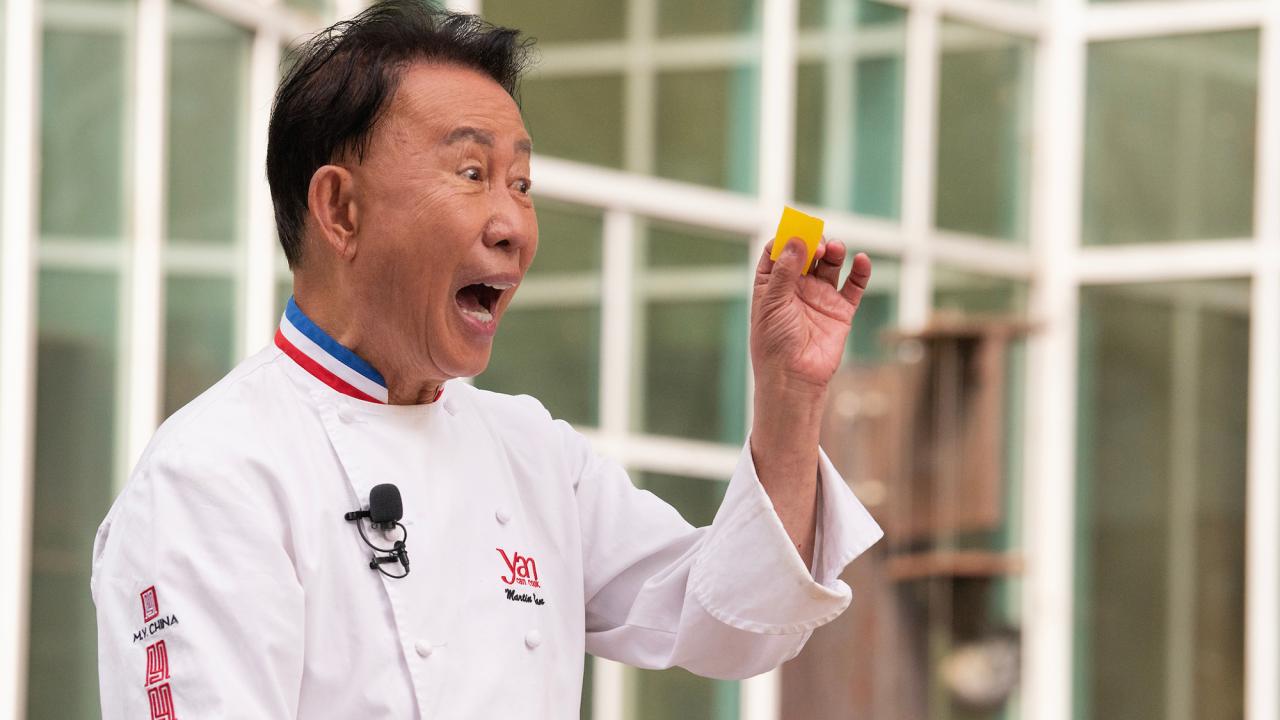 In his chef coat, celebrity chef Martin Yan holds up a piece of food