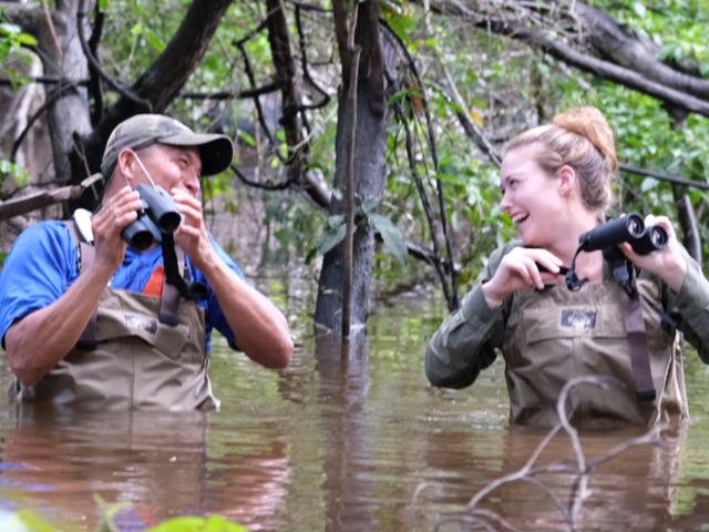 Two people are chest deep in flood waters in the Amazon rainforest.