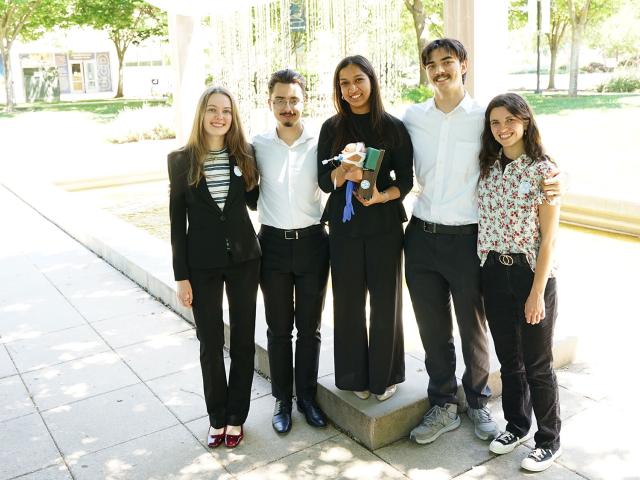 Six students in casual clothing standing by a courtyard fountain, smiling