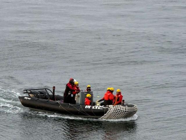 Eight scientists in coats and helmets ride in small boat in Antarctica  