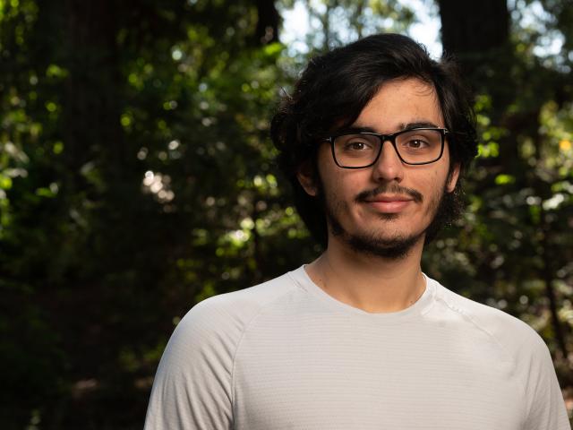 Casual outdoor portrait of a young man with glasses smiling against leafy background