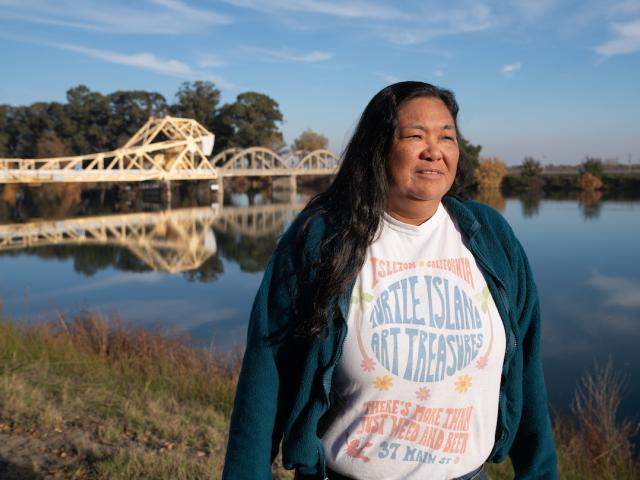 Pam Bulahan iin sweater and t-shirt stands with Sacramento River behind her