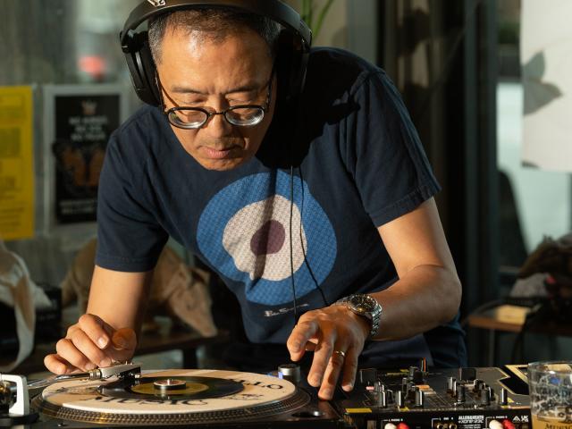 Man wearing headphones and blue target t-shirt adjusts vinyl on turntable in sunlit store