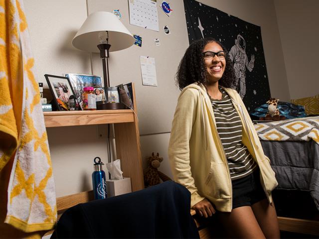 student leaning up against their desk in there residence hall room