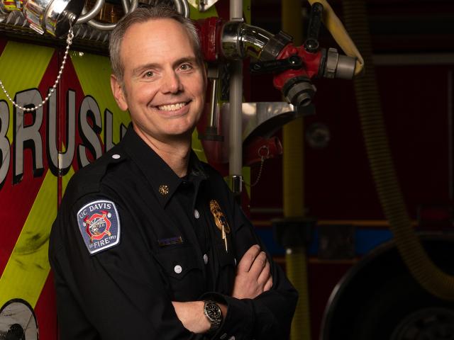 Fire chief stands in front of a fire truck with arms crossed.