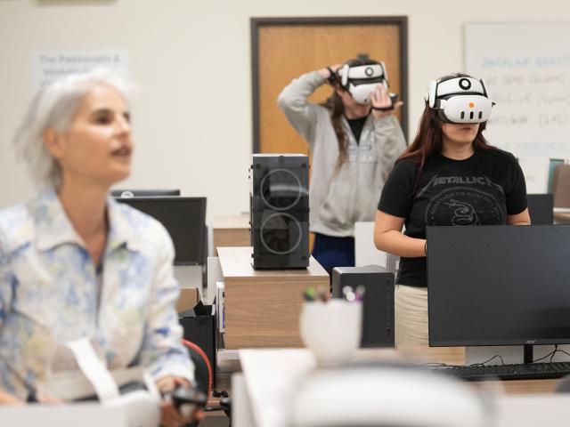 Classroom scene with two people wearing VR headsets at desks, instructor in foreground.