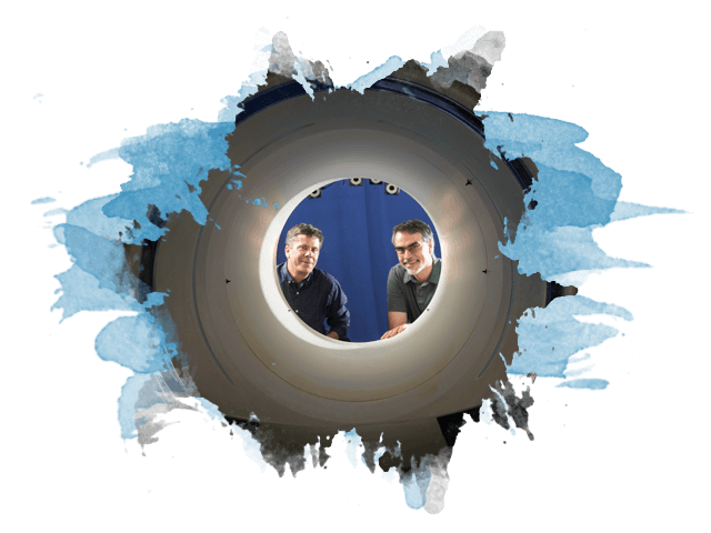 Two dudes look through the opening of a full body PET scanner