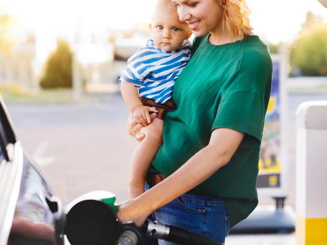 A mother holding a baby gasses up her car at the gas station