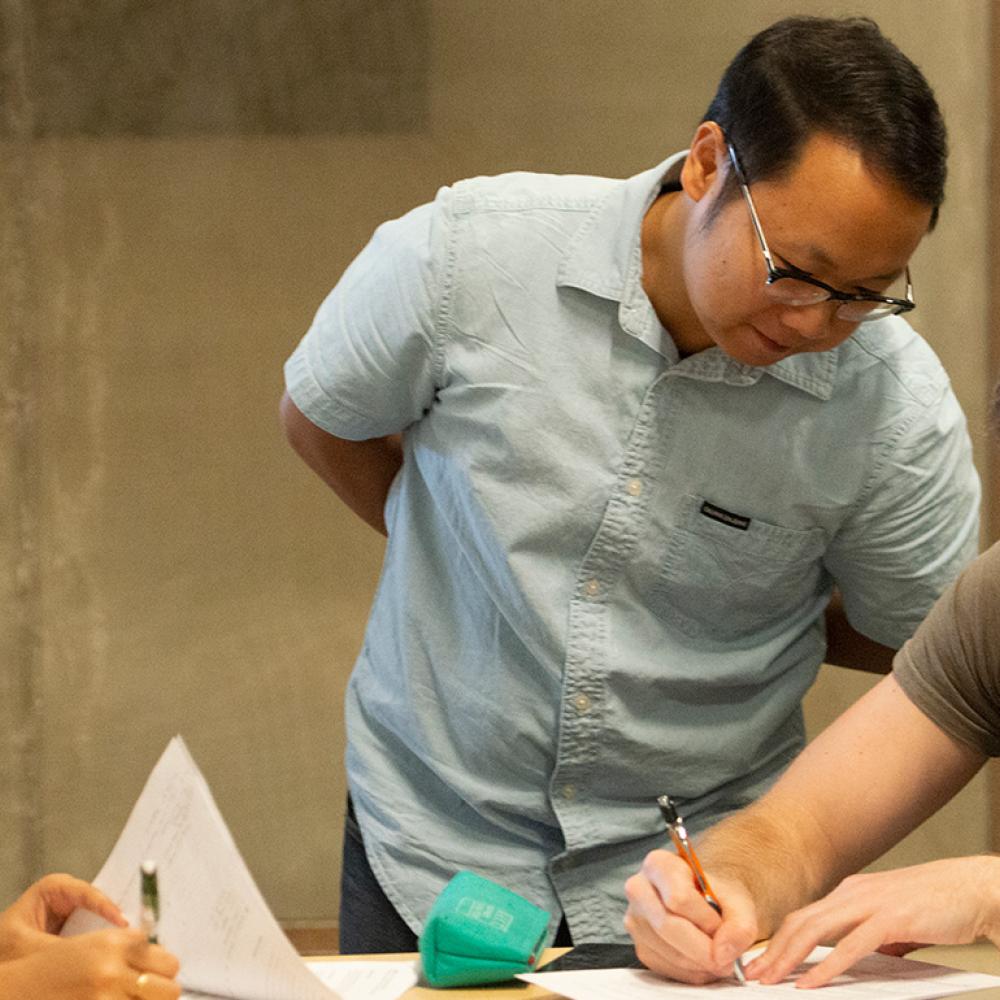 A teaching assistant leans over to assist a student during an engineering class.