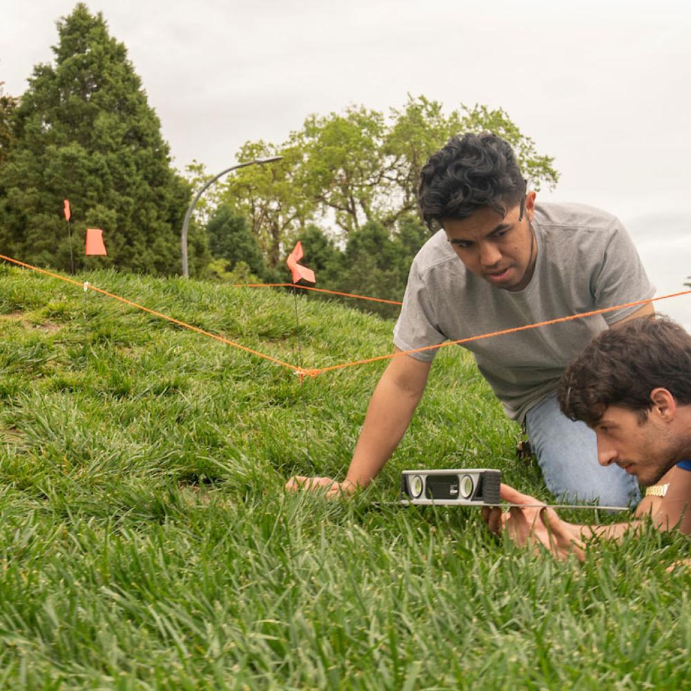 Two male students survey a landscape site with one of the UC Davis eggheads in the background
