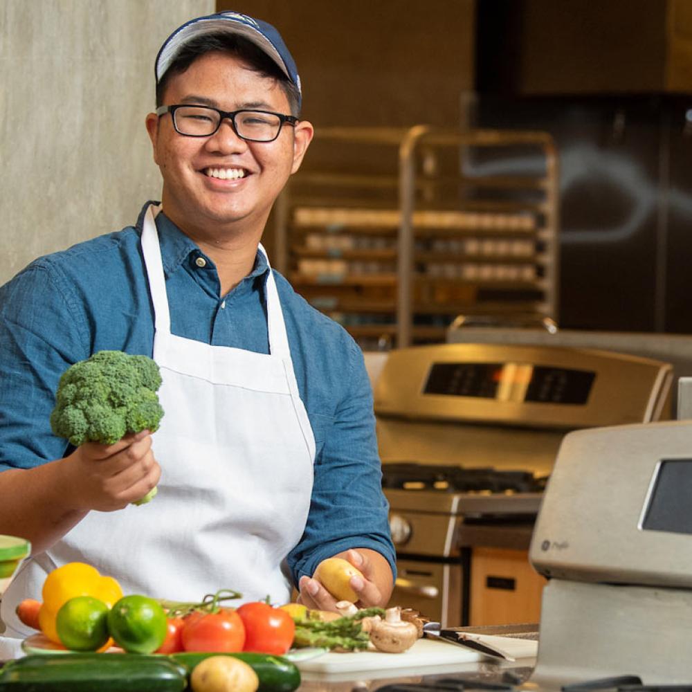 A male student poses with fruits and veggies in the research kitchen
