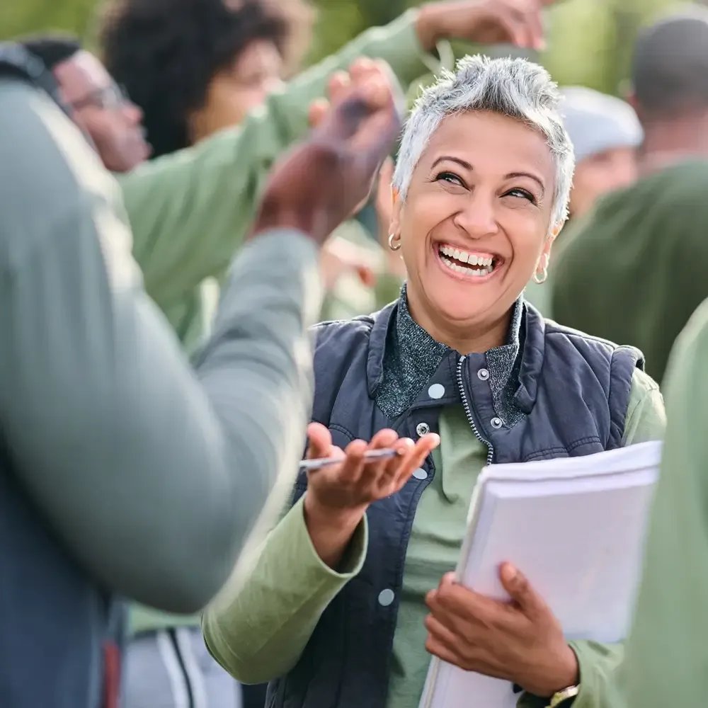 Smiling older woman with short gray hair holding notebooks, chatting outdoors