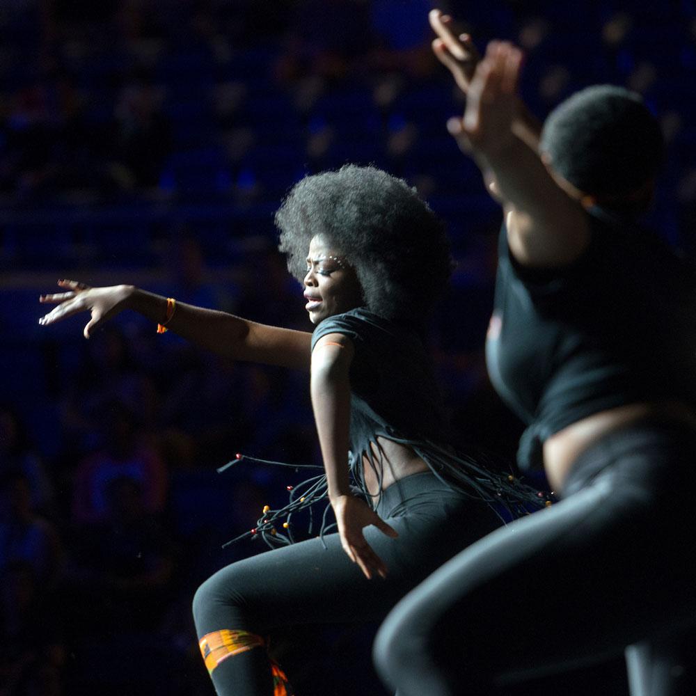 Two dancers on dark stage; woman with large afro striking dramatic pose