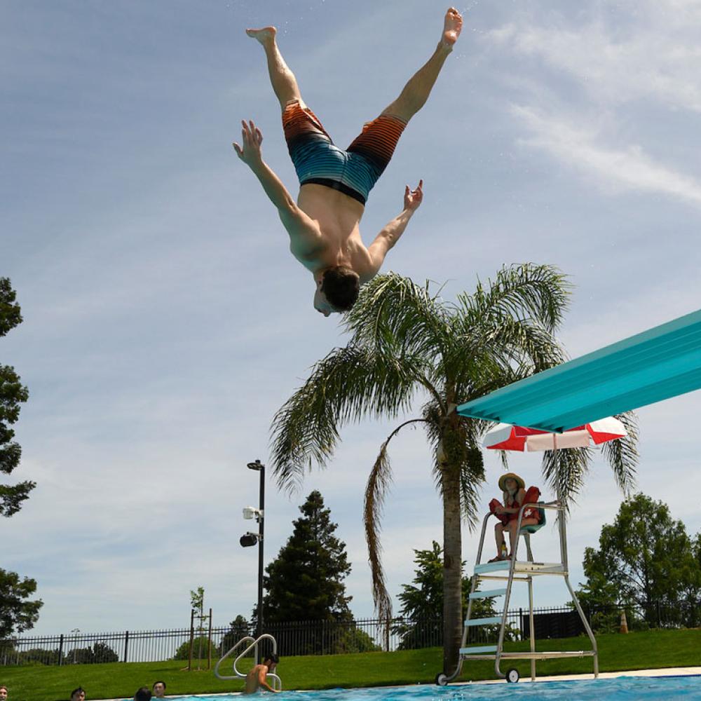A student doing an acrobatic jump of of the diving board at the UC Davis Recreation Pool
