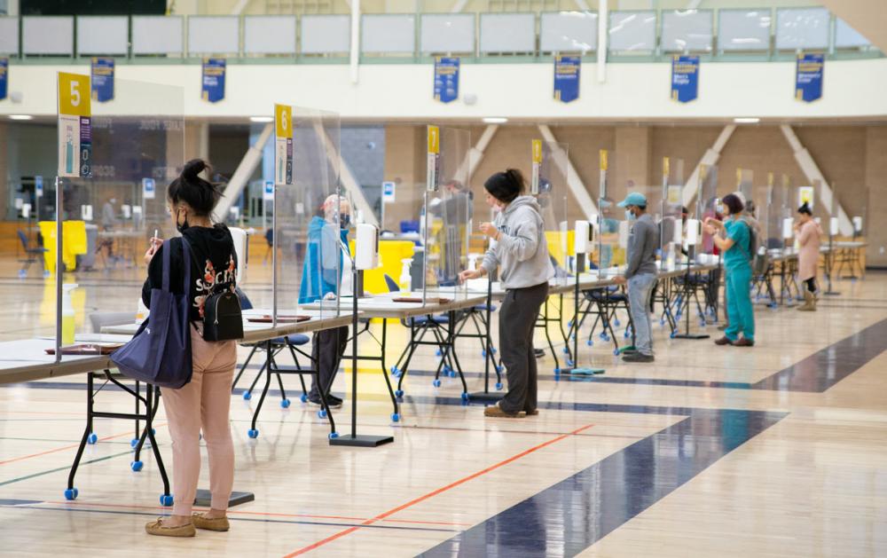 Long counter in gym with plastic dividers separating employees from people submitting saloiva samples.