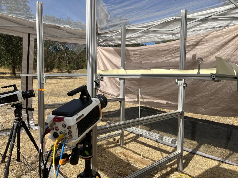 Two video cameras point towards a metal track, located in a metal frame tent outdoors.