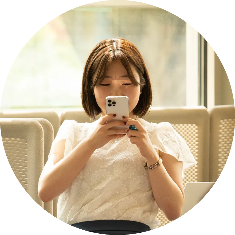 Young woman in white blouse seated by a sunlit window, focused on her smartphone.
