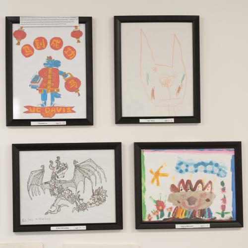 Four framed children's artworks displayed on a wall, featuring colorful illustrations.