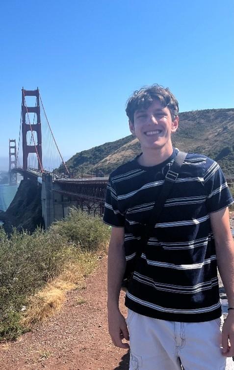 Derek Hernandez wears a blue striped shirt and poses for a picture  in front of the Golden Gate Bridge in San Francisco. 