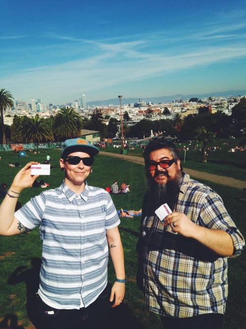 Eli holds up a card in a sunny park.