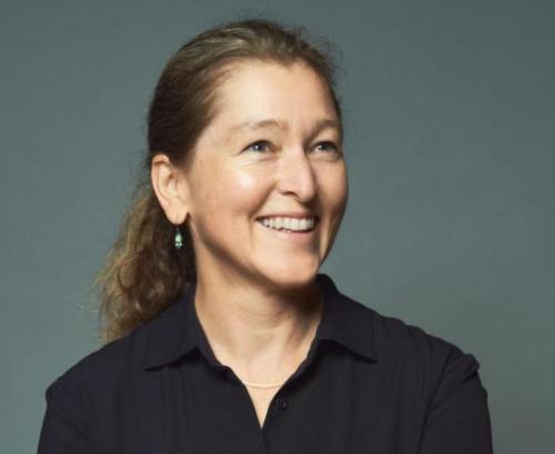 A headshot of a woman with brown hair and a black shirt against a grey background smiling away from the camera.