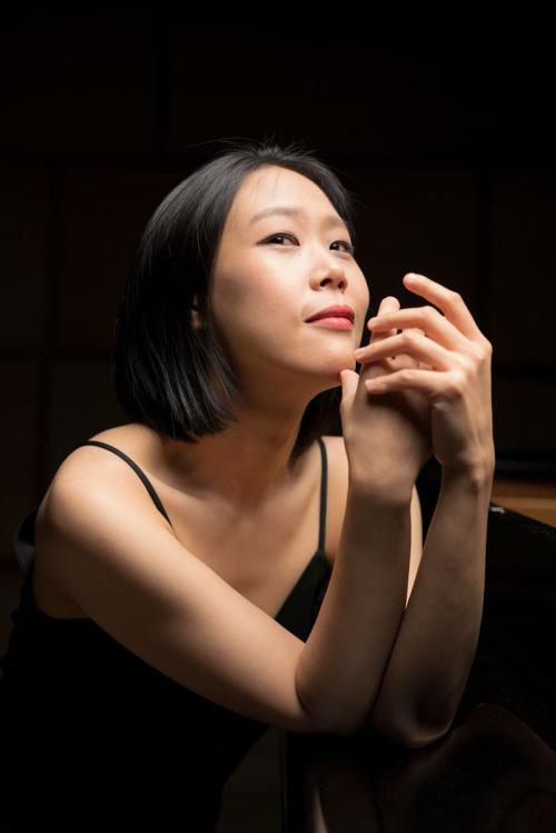 Studio portrait of contemplative woman in black tank top, hands near face, dramatic lighting