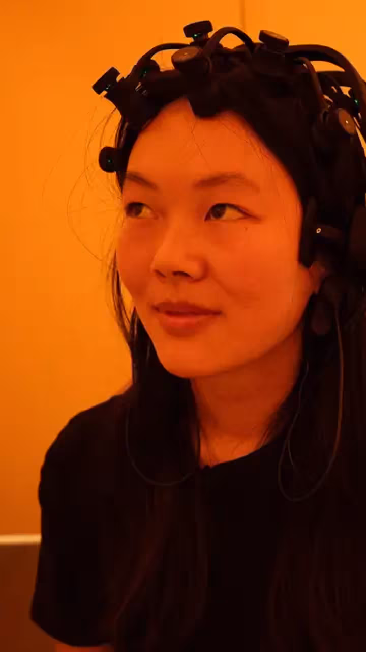 Woman with a specially designed headset in orange-lit room; man at laptop behind (photo)