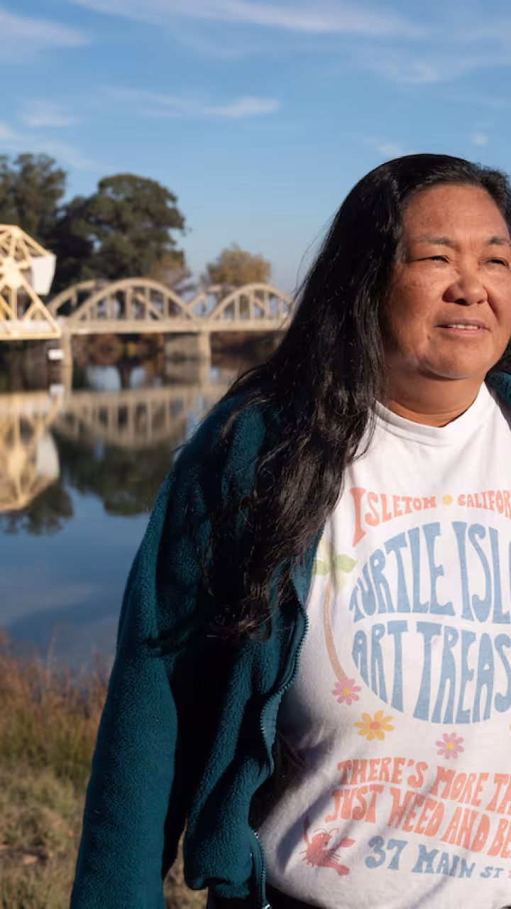 Pam Bulahan iin sweater and t-shirt stands with Sacramento River behind her