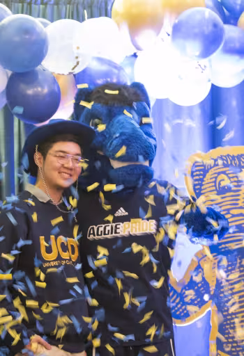 An incoming Aggie celebrating with Gunrock while another student takes their picture. 