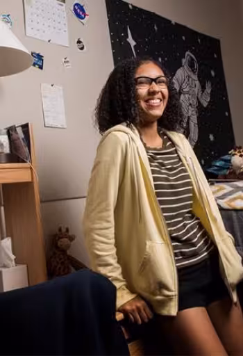 Student leaning up against their desk in there residence hall room