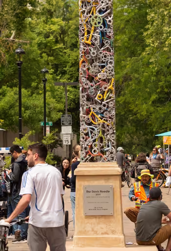 A scene of downtown Davis, Ca, full of students, locals and a unique obelisk shaped sculpture made of bicycle parts