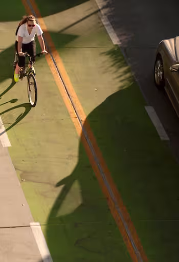 a female student rides her bike through a clearly marked green bike line next to a car on the UC Davis campus