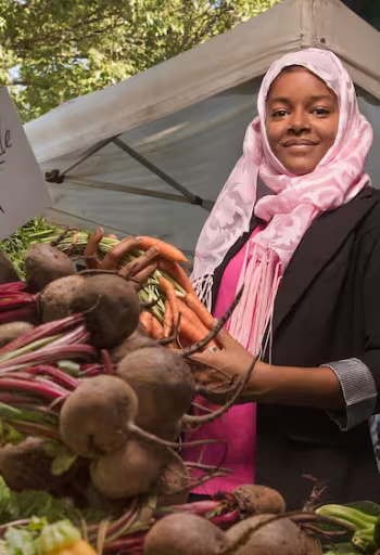 A female student picks up some veggies at the Davis Farmer's Market