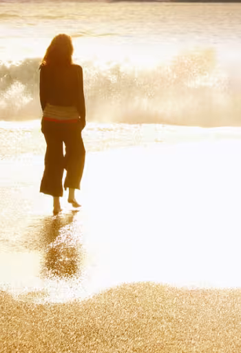 A woman stands on the beach at sunset