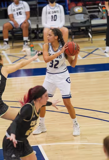 Female basketball player #32 in white readies a pass on indoor court with defenders nearby.