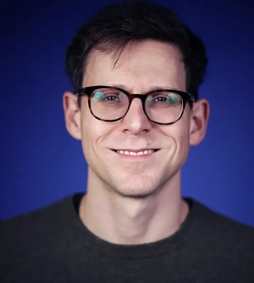 A smiling person with glasses against a blue background.