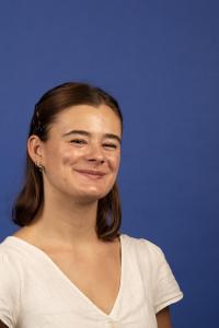 A person in a white shirt, smiles for a portrait in front a plain blue background.
