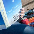 Woman reading a book by Pam Houston on a bench with other books, a can of pop and sunglasses