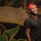 student posing for a photo in front of a wall with a painting