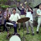 Sammy Miller and the Congregation joyfully playing theor musical instruments in a grassy backyard.