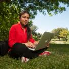 A student sits in the grass cross-legged with her laptop in 2017. 