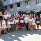 Students hold up their degrees in a cluster of 25 people. 