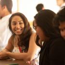 Two students smile at each other in a sunny classroom. 