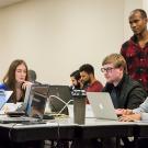 Instructor Nelly Sugira, standing to the right, helps students with a code-stringing exercise 