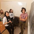 Five male and femal students looking at a blackboard