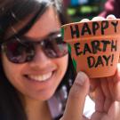 A woman holds up a painting that reads Happy Earth Day