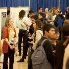 A woman stands in front of a poster and talks with others at a crowded event