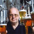 Photo: man posing with several glasses of beer with brewing facilities in background