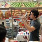 Man gesturing in front of a painted mural with two people watching him